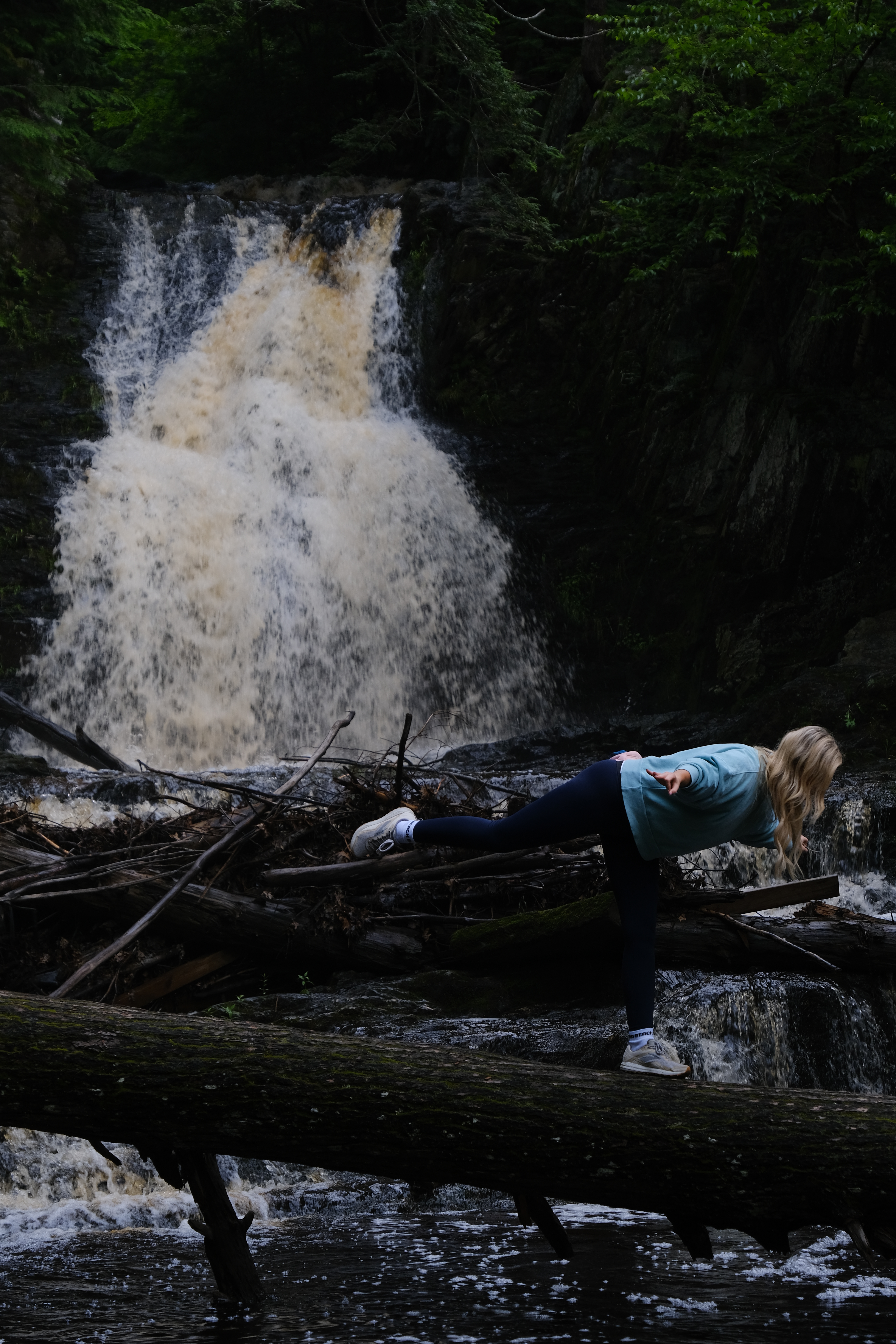 A professionally edited photo of a young woman performing a yoga pose in front of a beautiful waterfall.